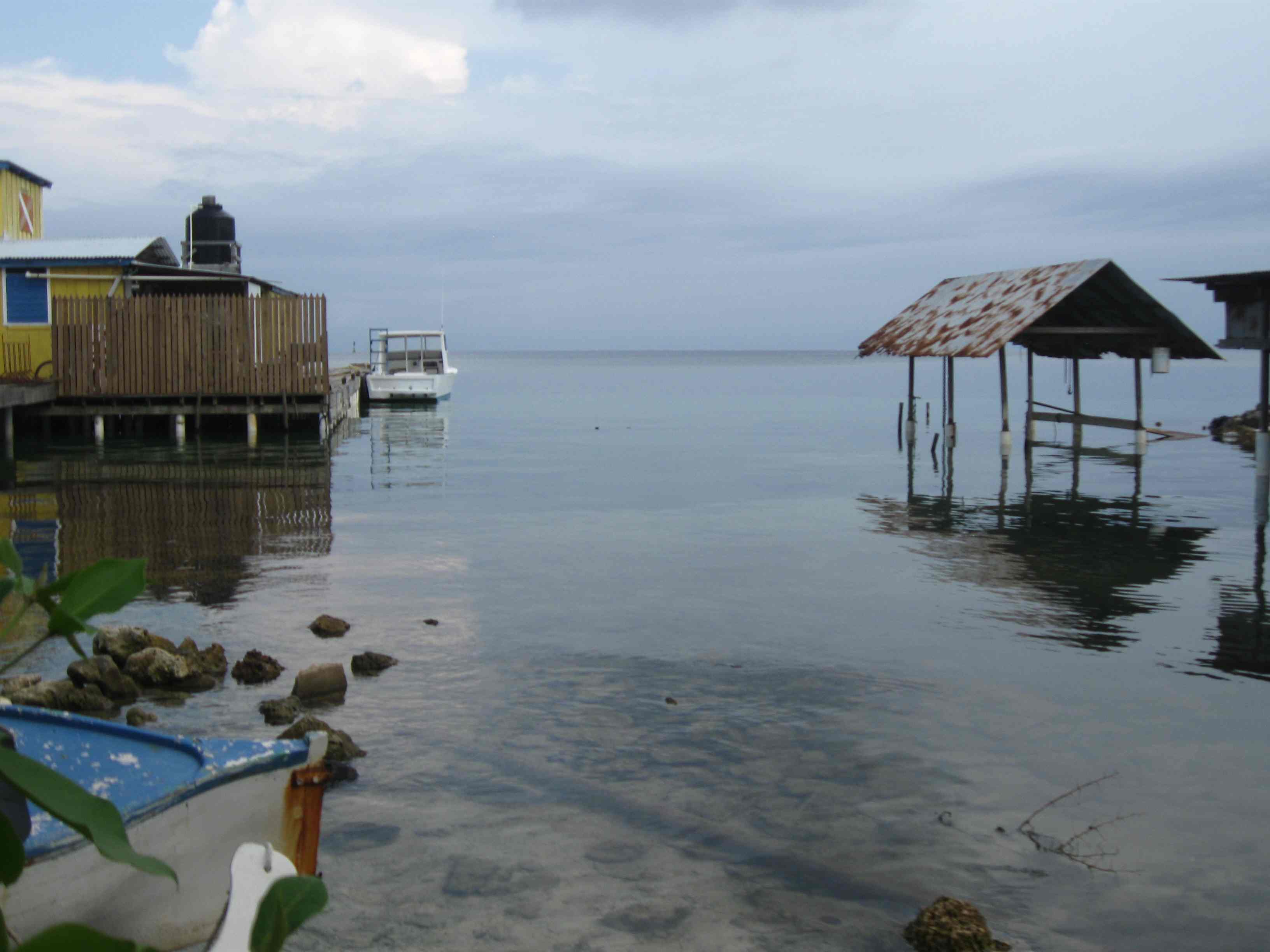 Wooden dock, stilt boathouse and a moored boat on calm water in Utila Town, Honduras