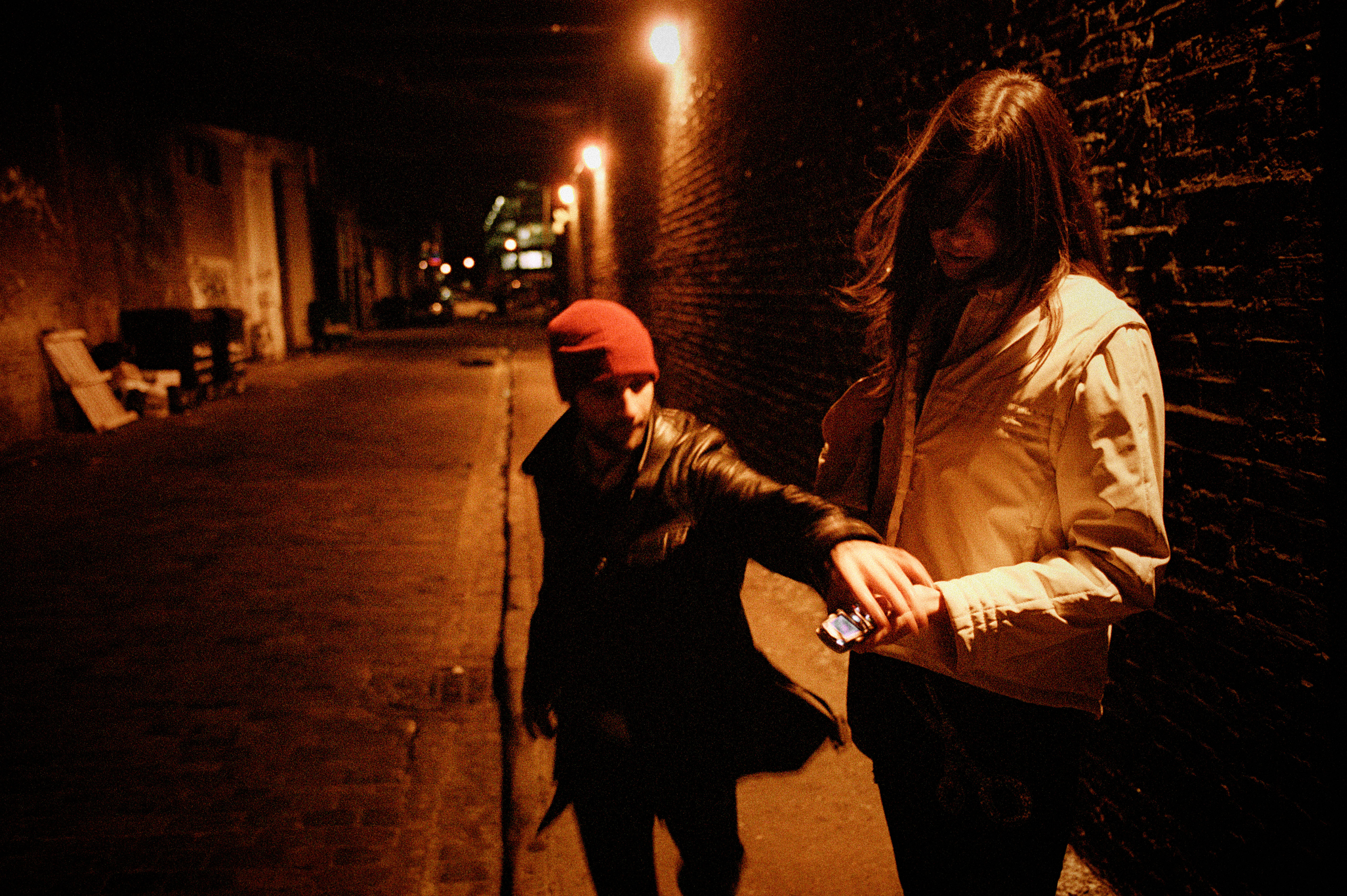 A man snatches a mobile phone from a woman in a dimly lit street POSED BY MODELS