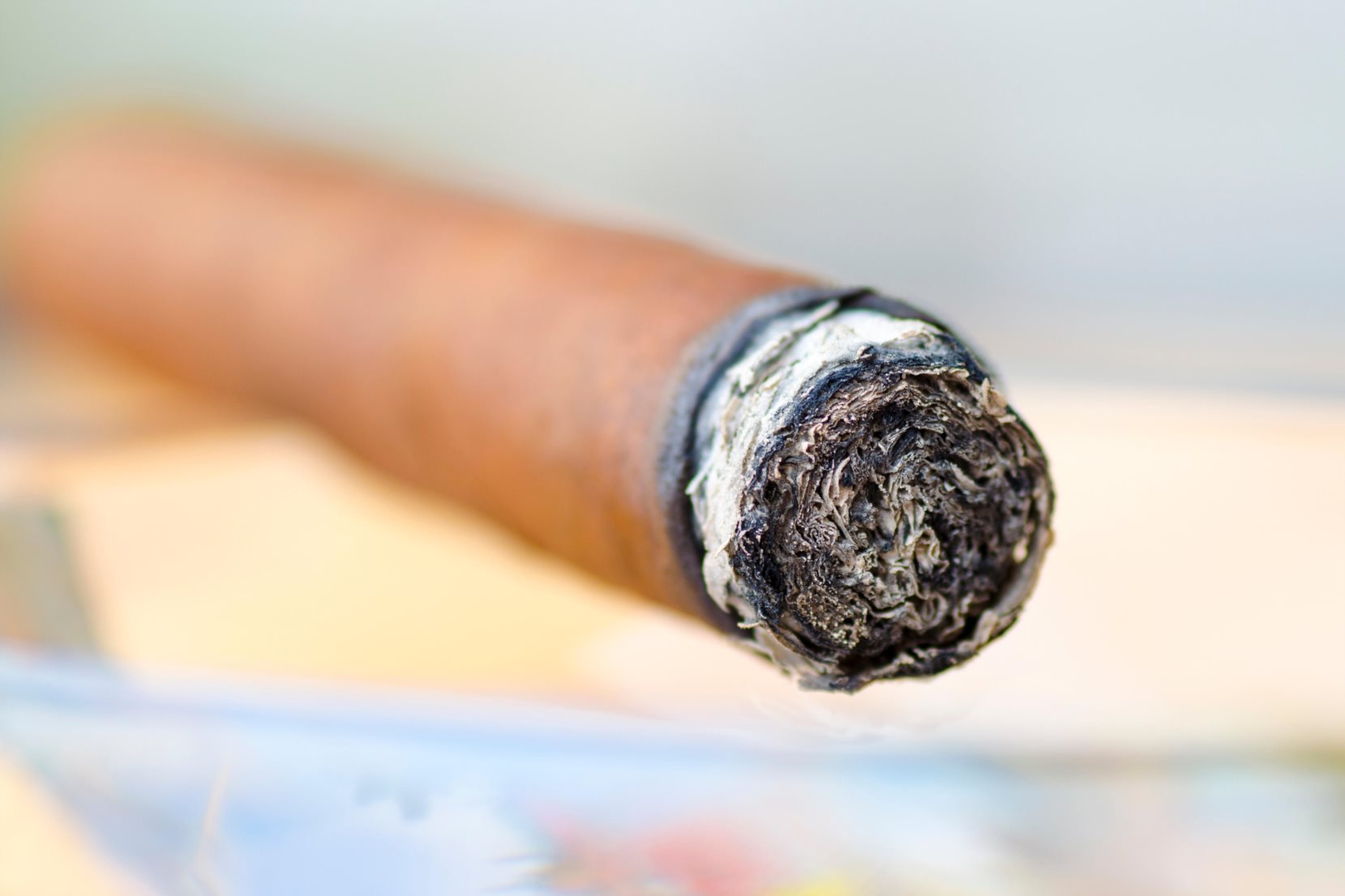 Close-up photo of a burning cigar in a glass ashtray with a blurred background