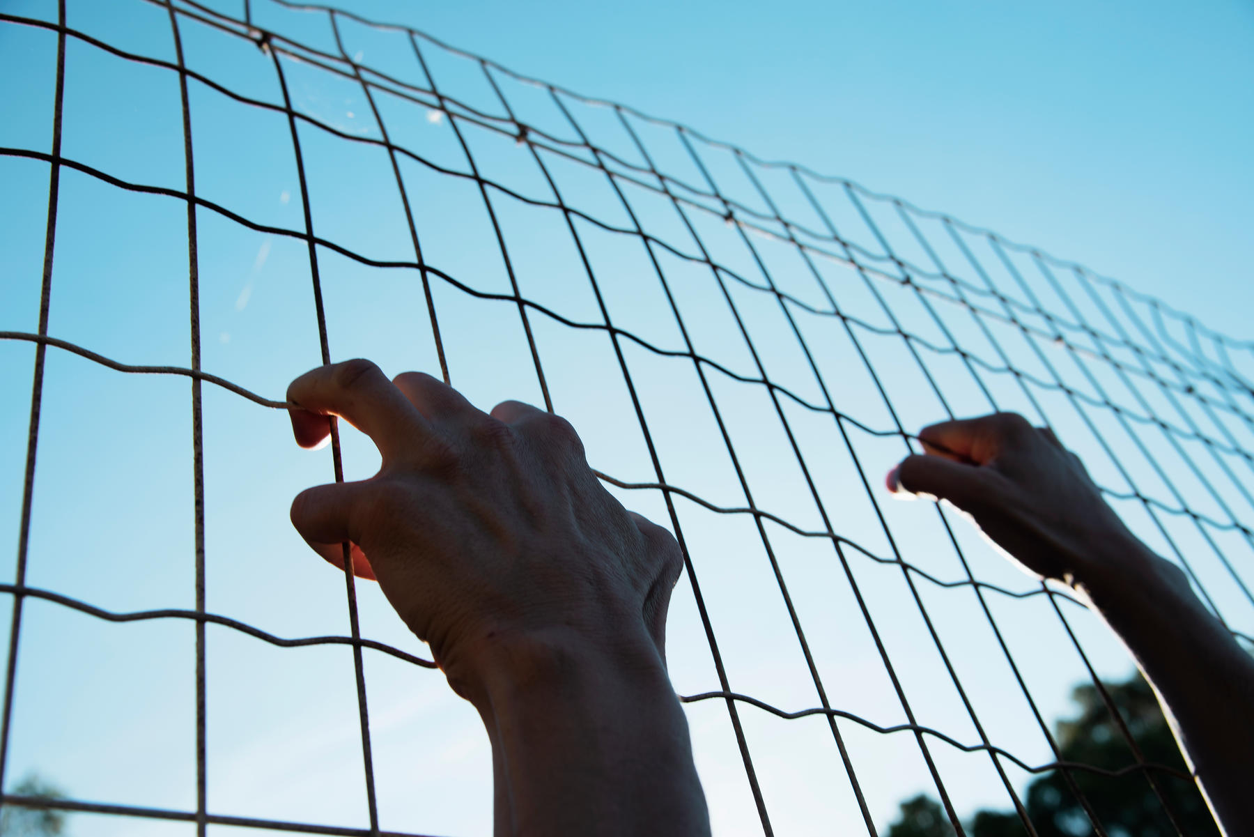 closeup of the hands of a man trying to climb up a metal fence