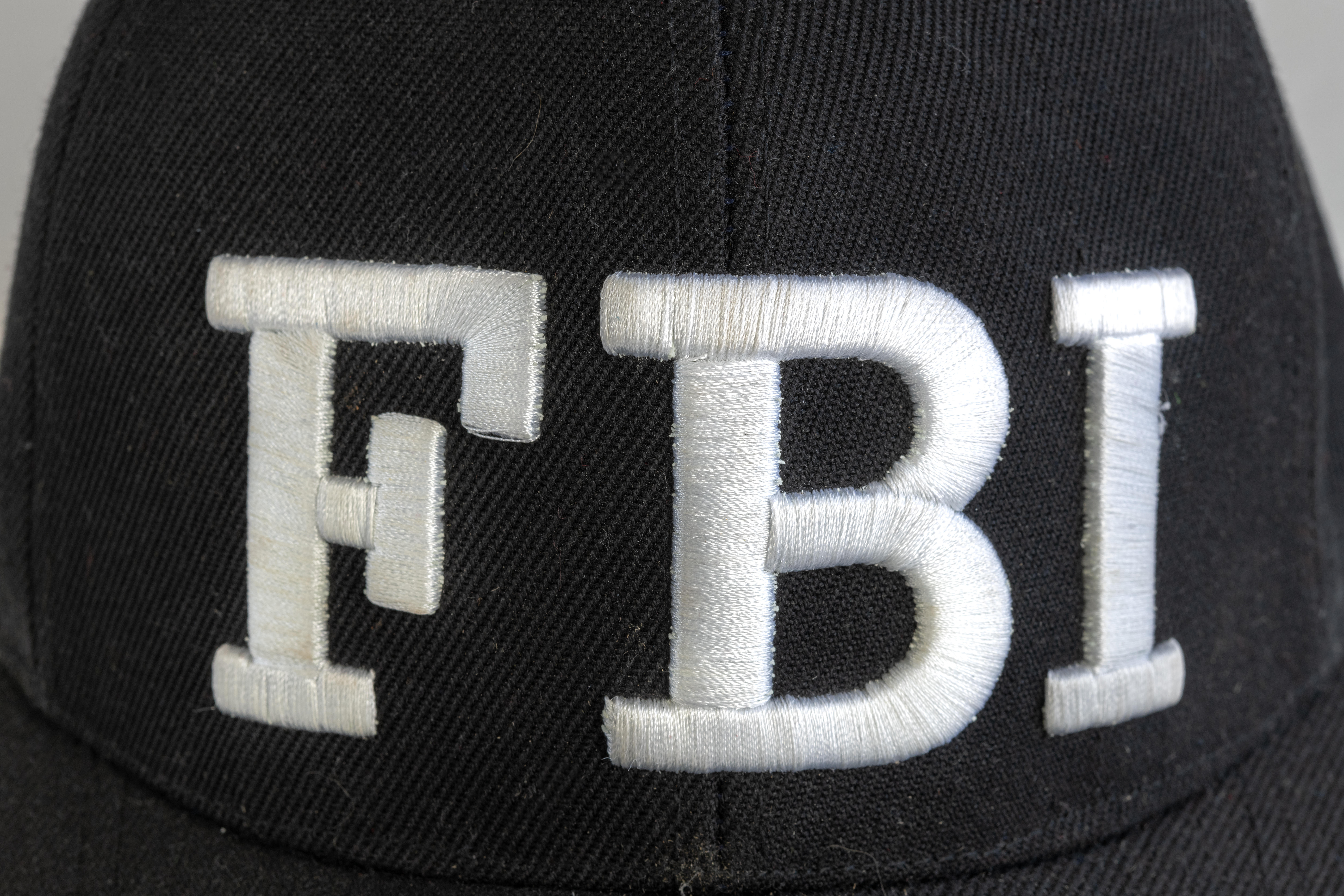Close up of the FBI logo on a black cap. The text stands for Federal Bureau of Investigations. Frontal view.