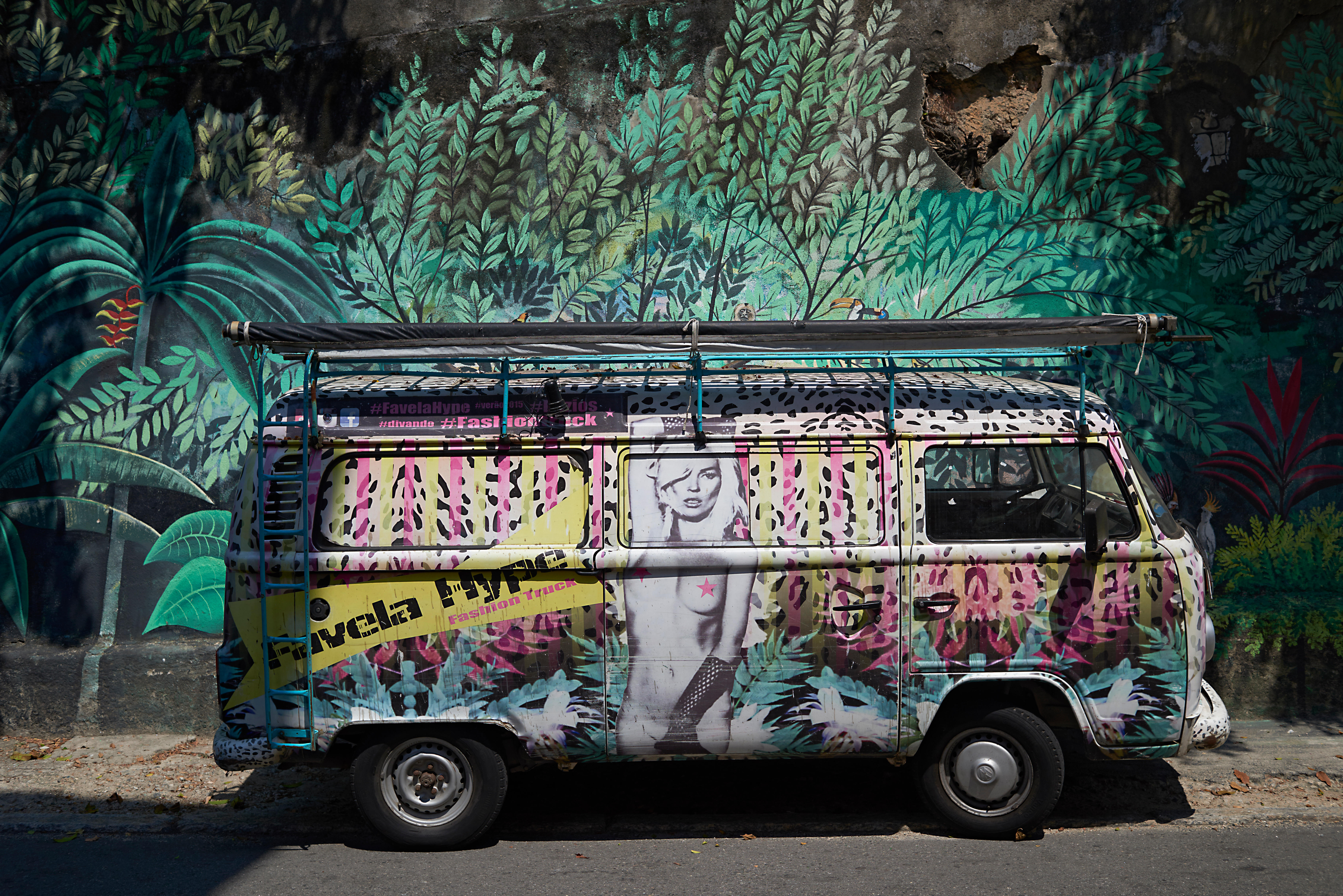 Side view of an old Volkswagen camper van painted in bright colors and blending in with the painted walls behind
