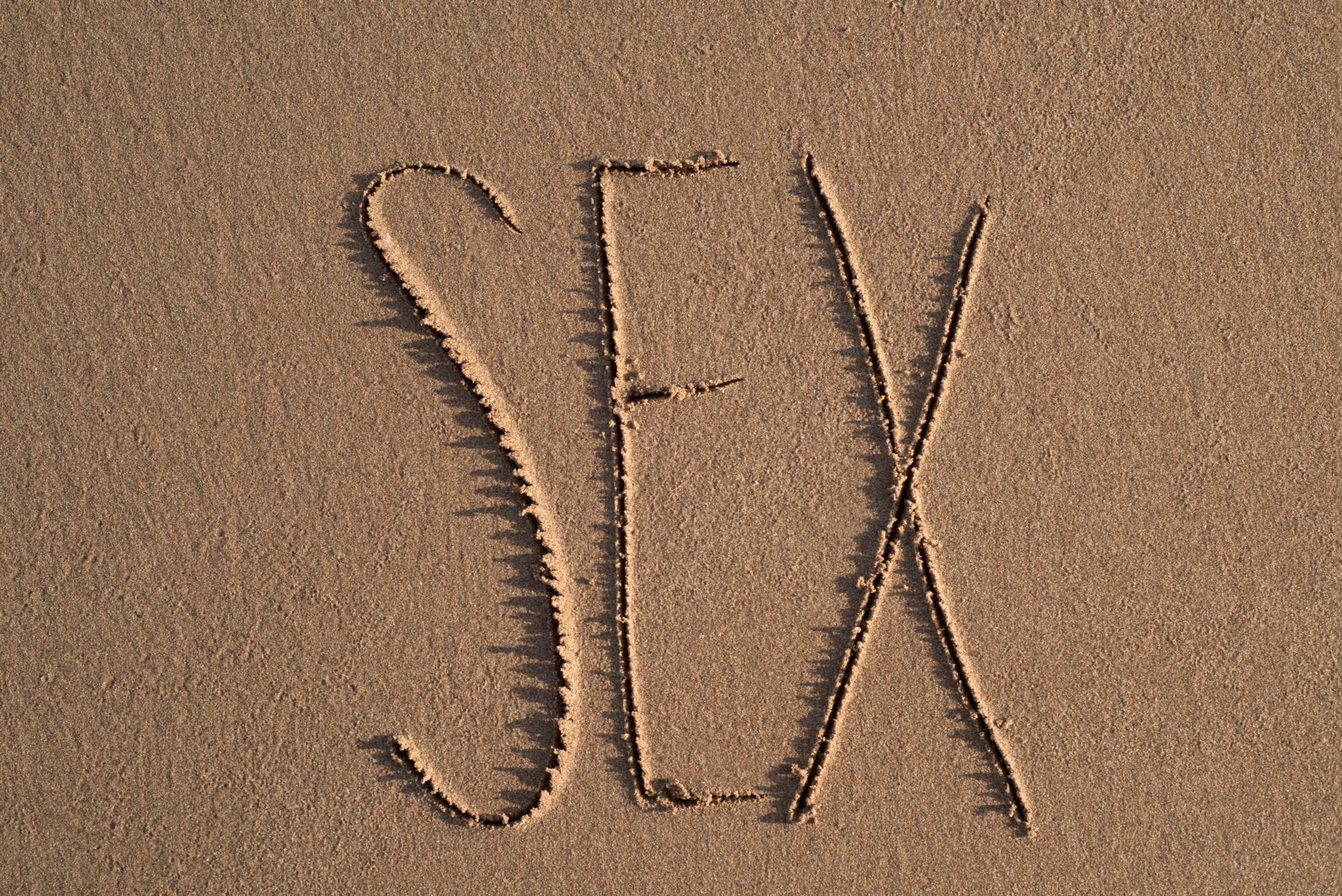 high-angle shot of the word sex written on the sand of a beach