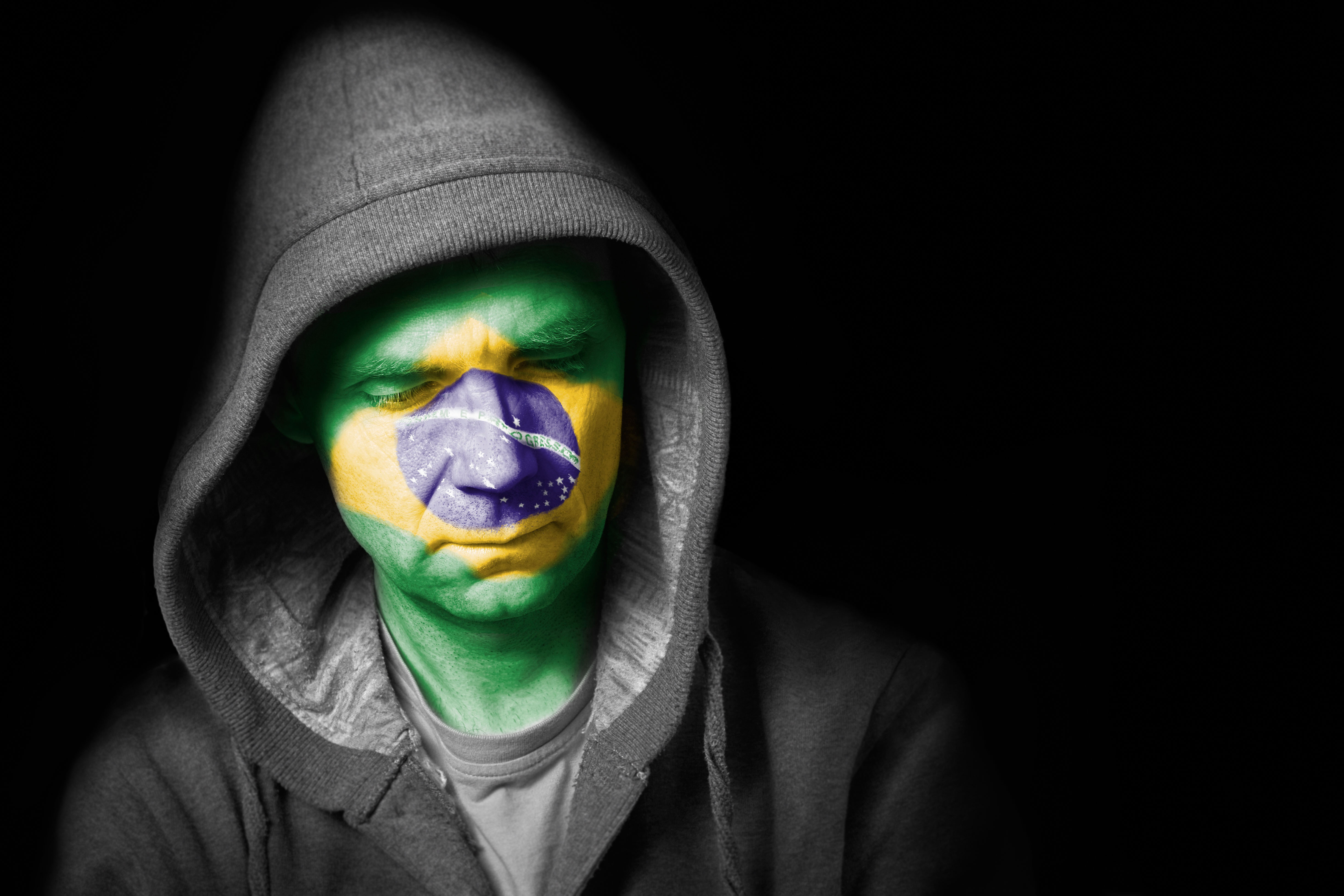 A sad expression on the face of a football fan with their face painted with the Brazilian flag.