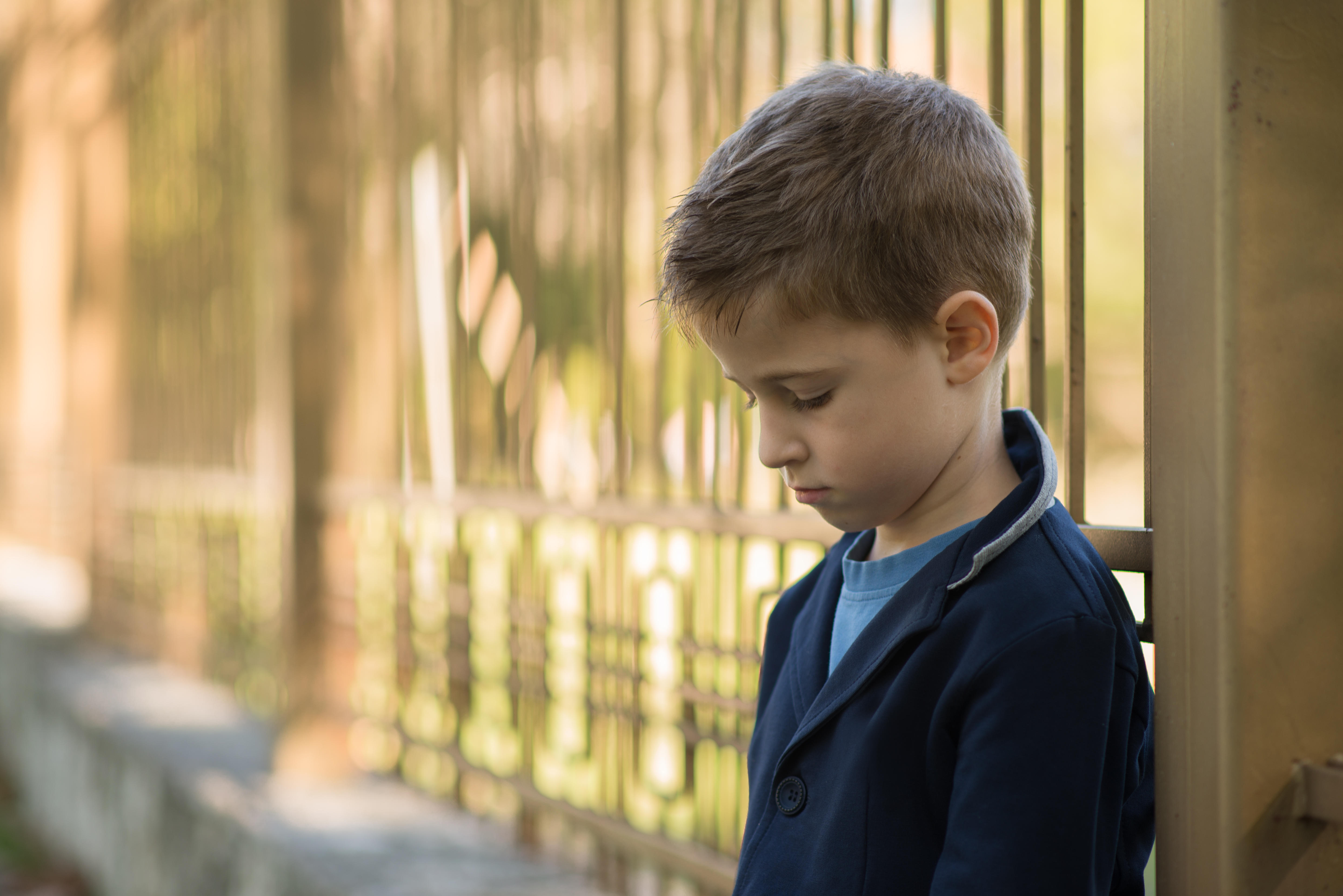 Portrait of a sad boy leaning against metal railings