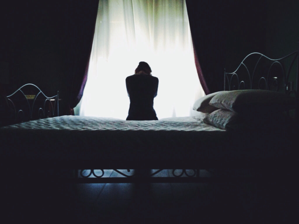 Rear View Of Woman Sitting On Bed Against Curtain