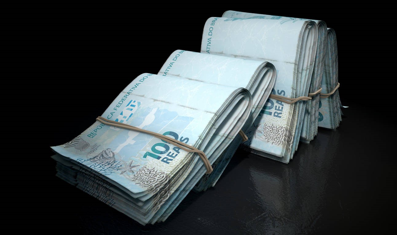 A close-up view of five wads of folded over stacks of brazilian real banknotes each bound informally by a rubber band set out