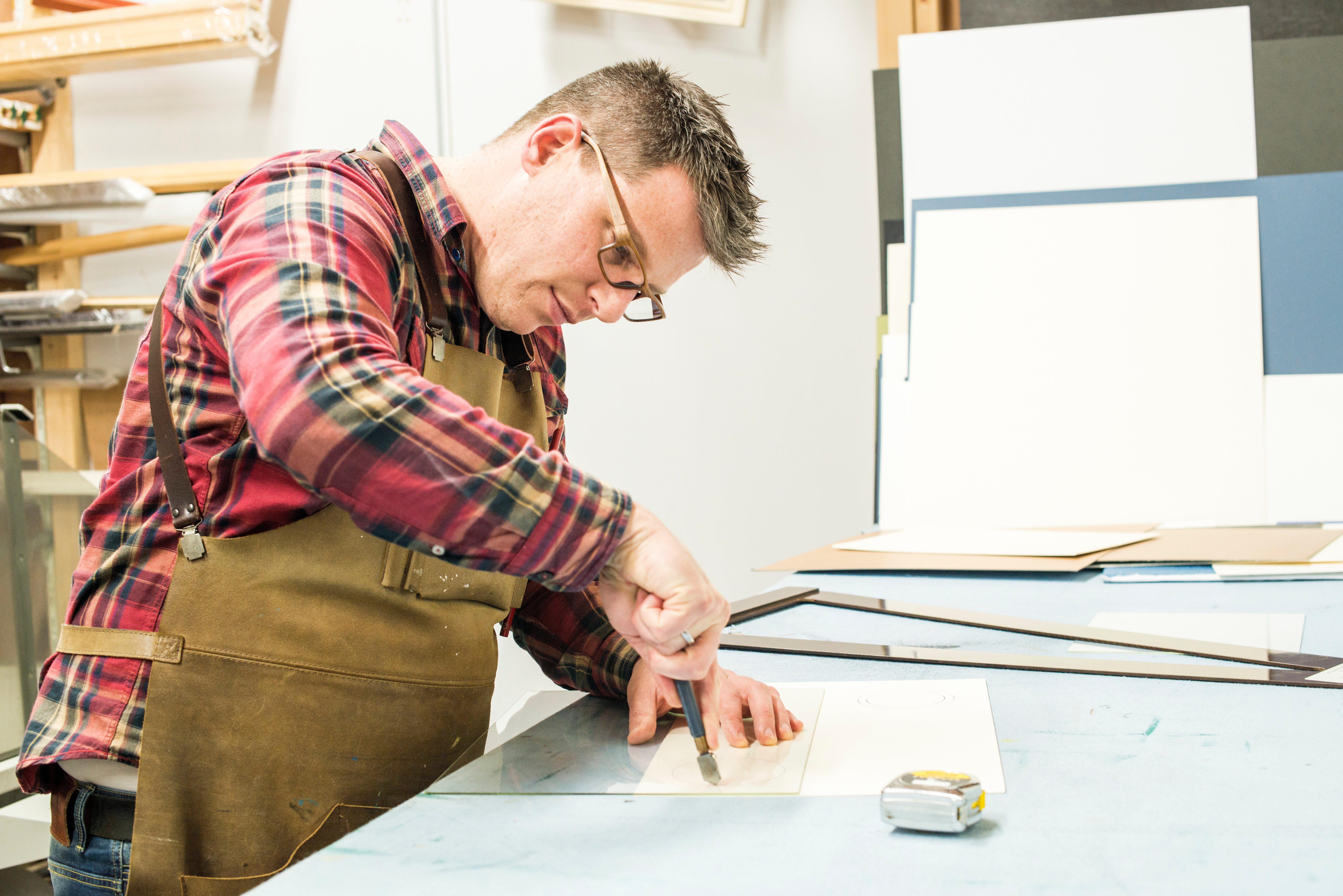 Goirle, Netherlands. Mid adult male craftsman and picture framemaker, cutting up sheets of glass for a new picture frame.