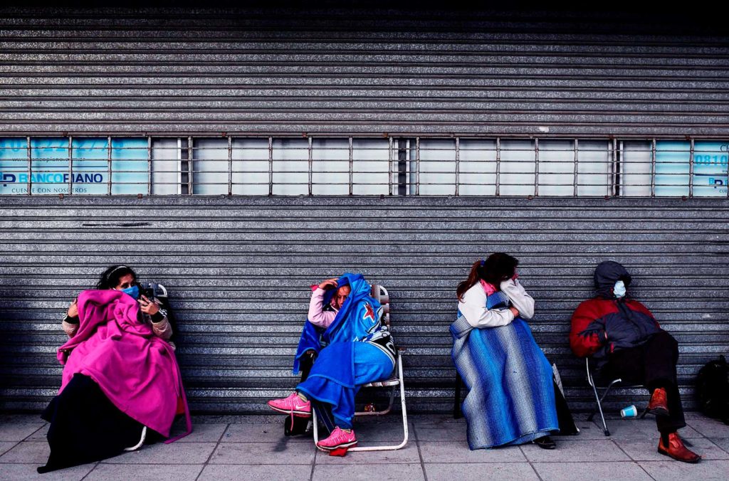 People wrapped in blankets sitting outside a closed bank