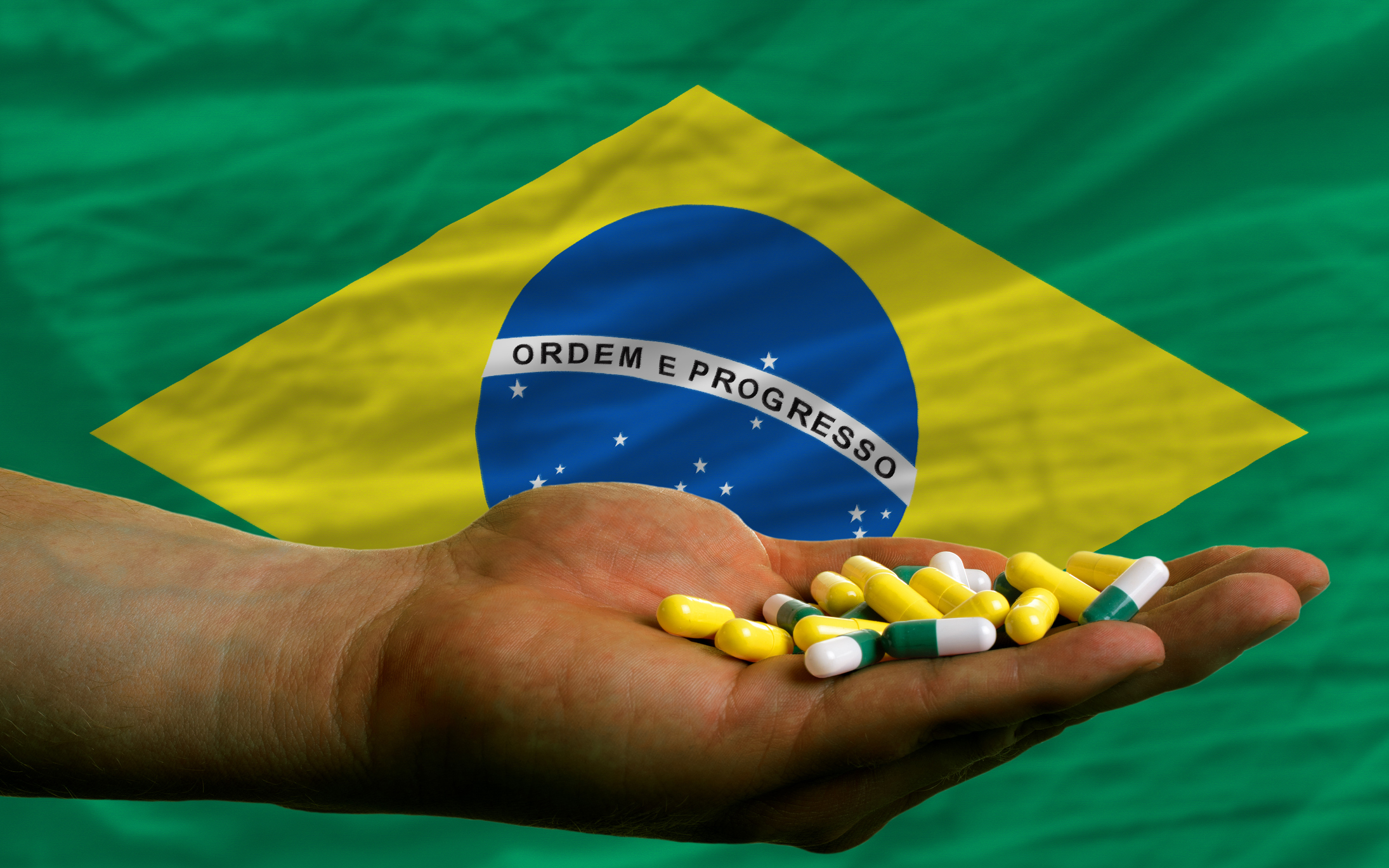 holding pills in hand in front of brazil national flag