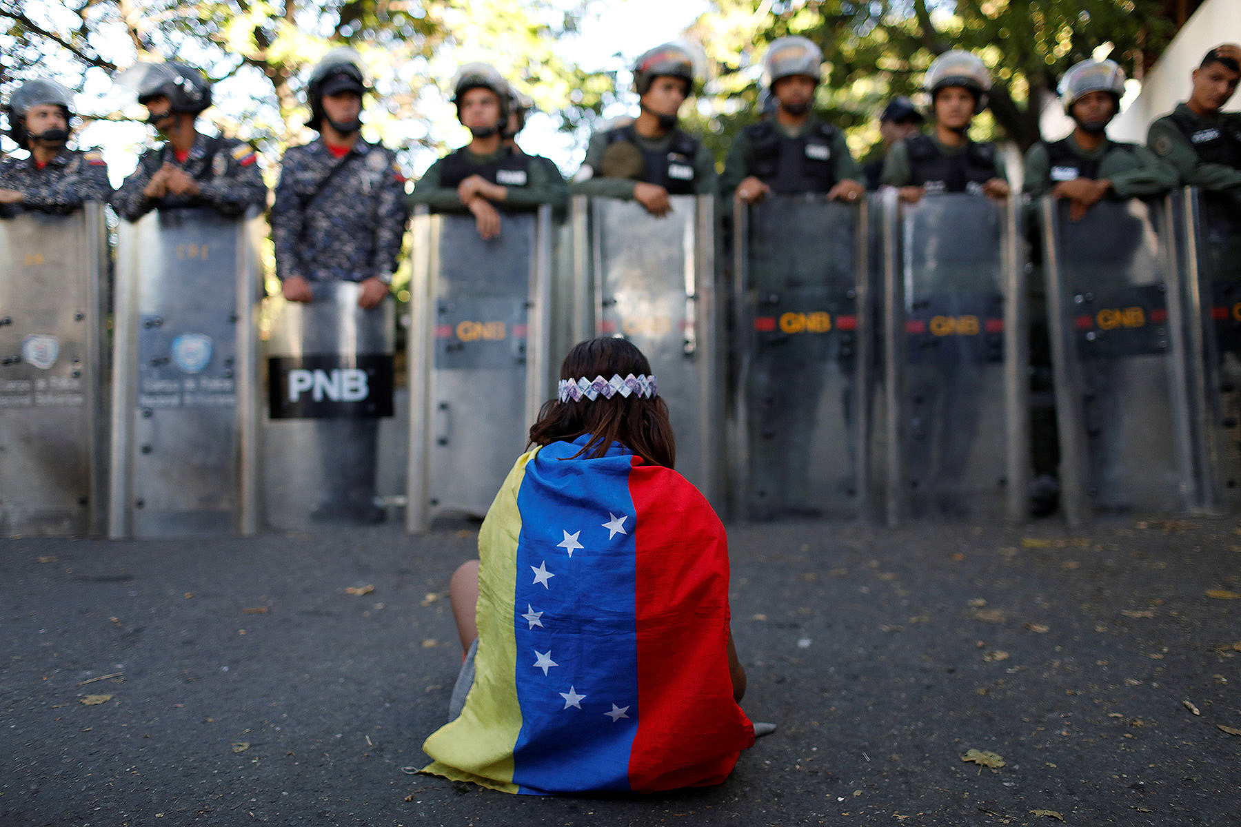 A girl wears a Venezuelan flag as Venezuelan security forces block access to opposition supporters and mourners of rogue ex-policeman Oscar Perez to the main morgue of the city, in Caracas