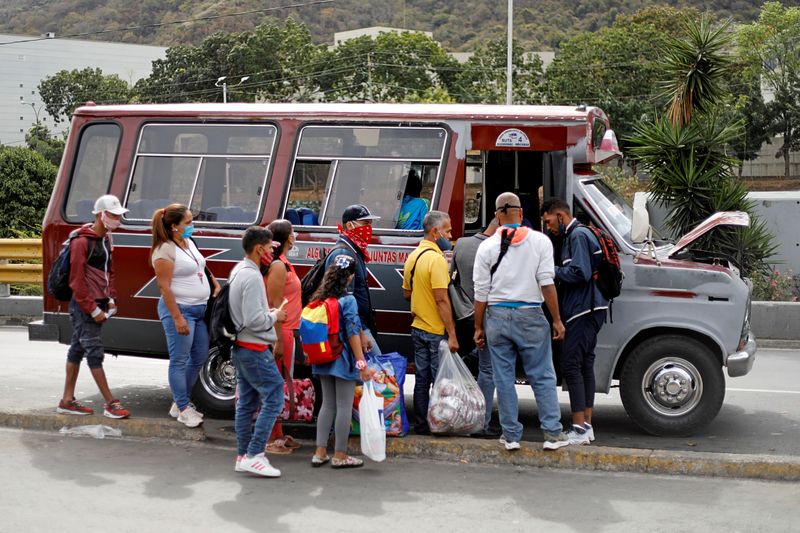 People queue to board a bus as the bus driver's assistant collects fares at a bus stop outside the Antimano metro station in Caracas