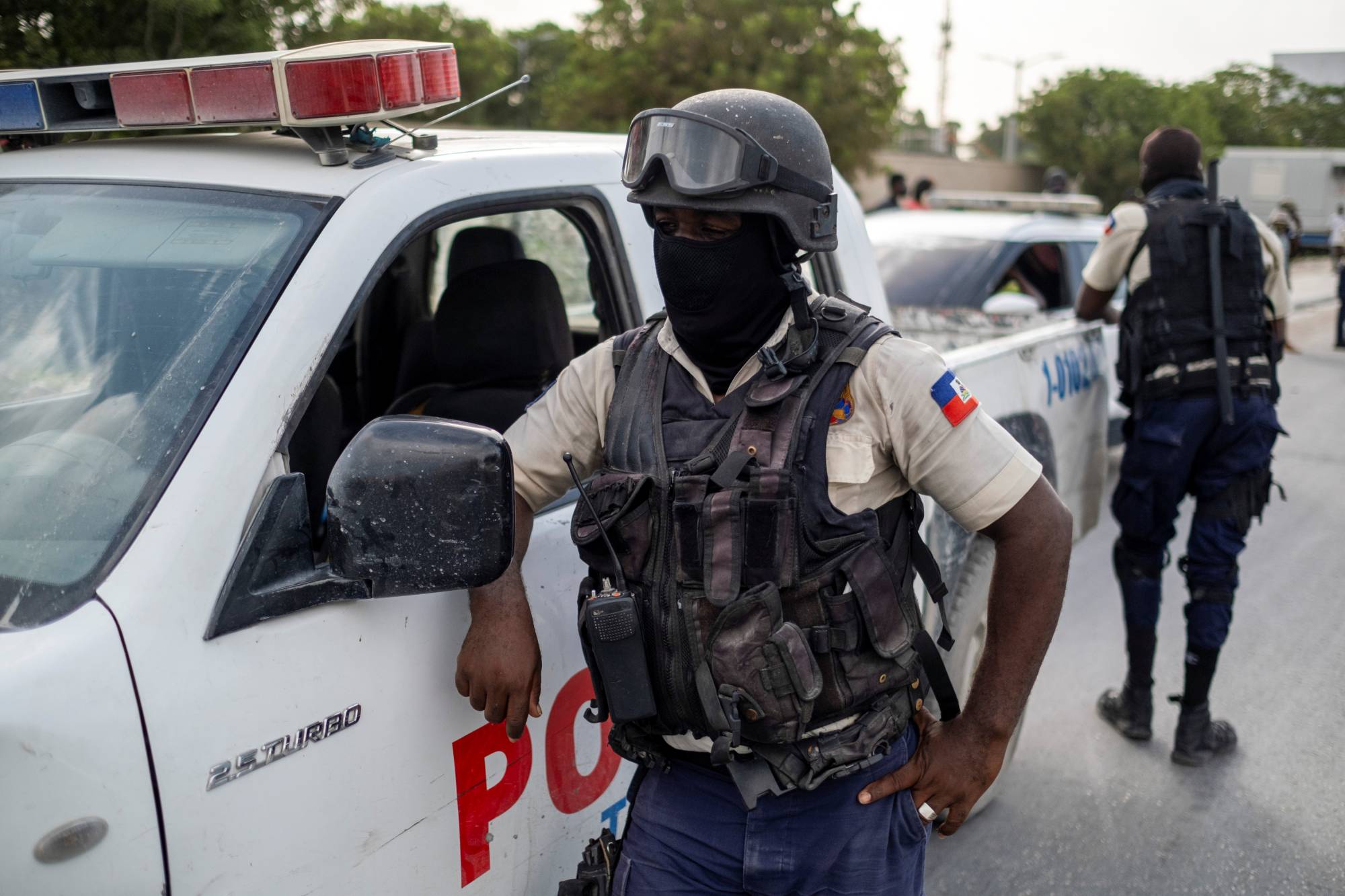 A masked Haitian National Police officer in body armour beside a police pickup in Port-au-Prince