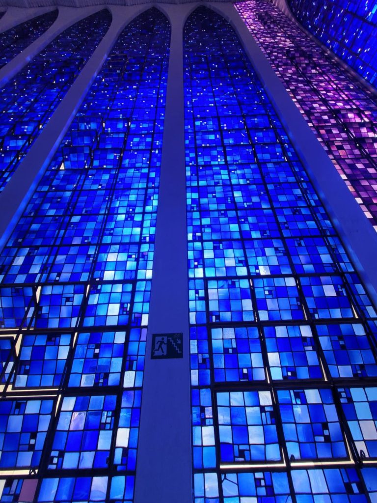 Pink stained glass at the four corners gives a preternatural frame to the 12 shades of blue to purplish-blue stained glass that fills the columns in some 140,000 squares designed by Sao Paulo architect Cláudio Naves and manufactured by the Belgian artist Hubert Van Doorne.