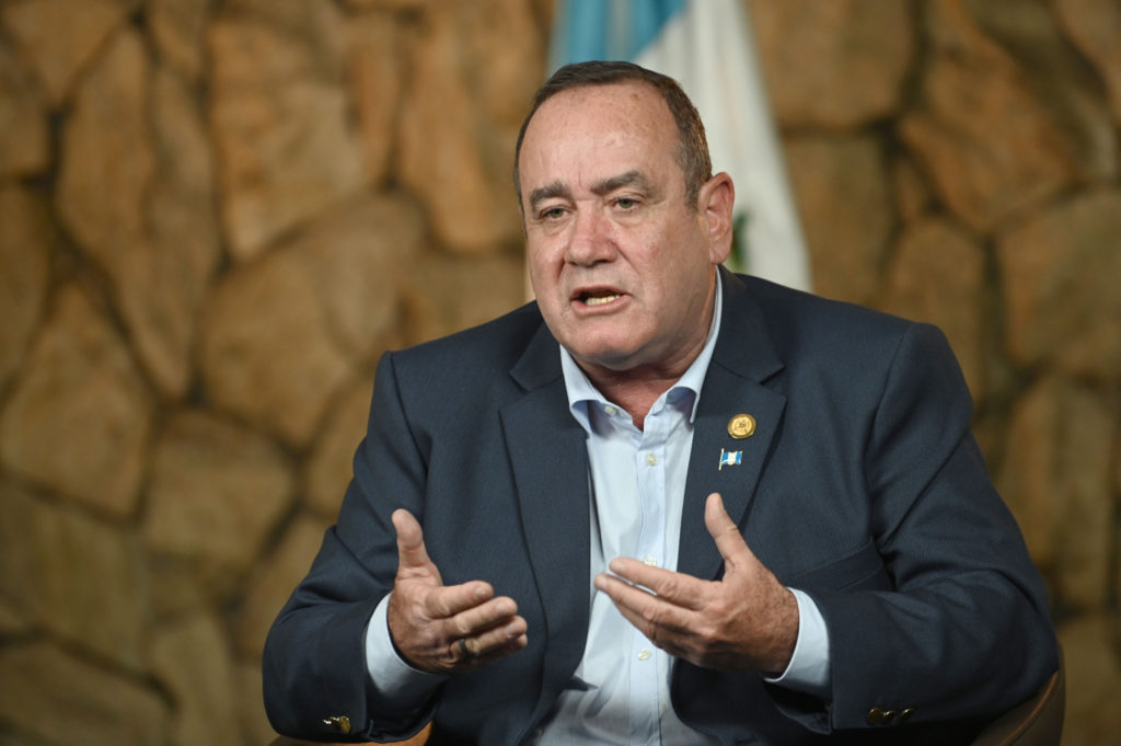 Man in suit speaking, Guatemala flag pin visible