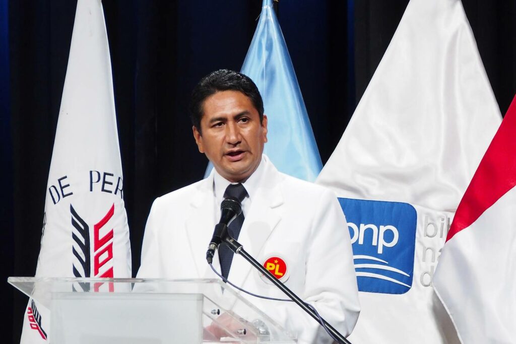 Man speaking at podium with flags, one says 'DE PERU'