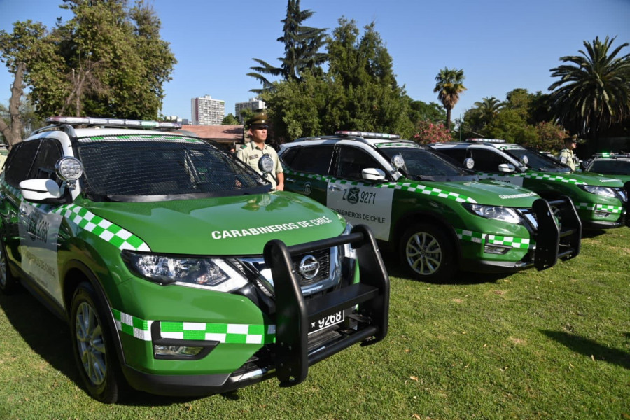 A row of green-and-white Carabineros de Chile patrol cars with an officer standing beside them