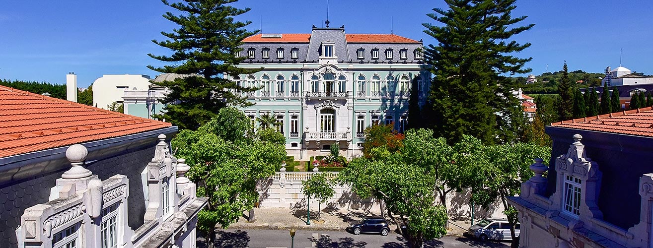 The pastel-green Pestana Palace seen over rooftops and pine trees in Lisbon, Portugal