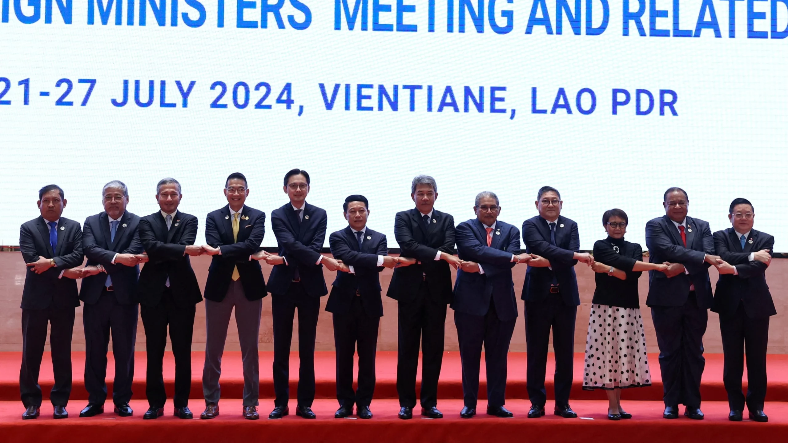 Defence ministers standing arm in arm on stage at the ADMM-Plus meeting in Vientiane, Laos.