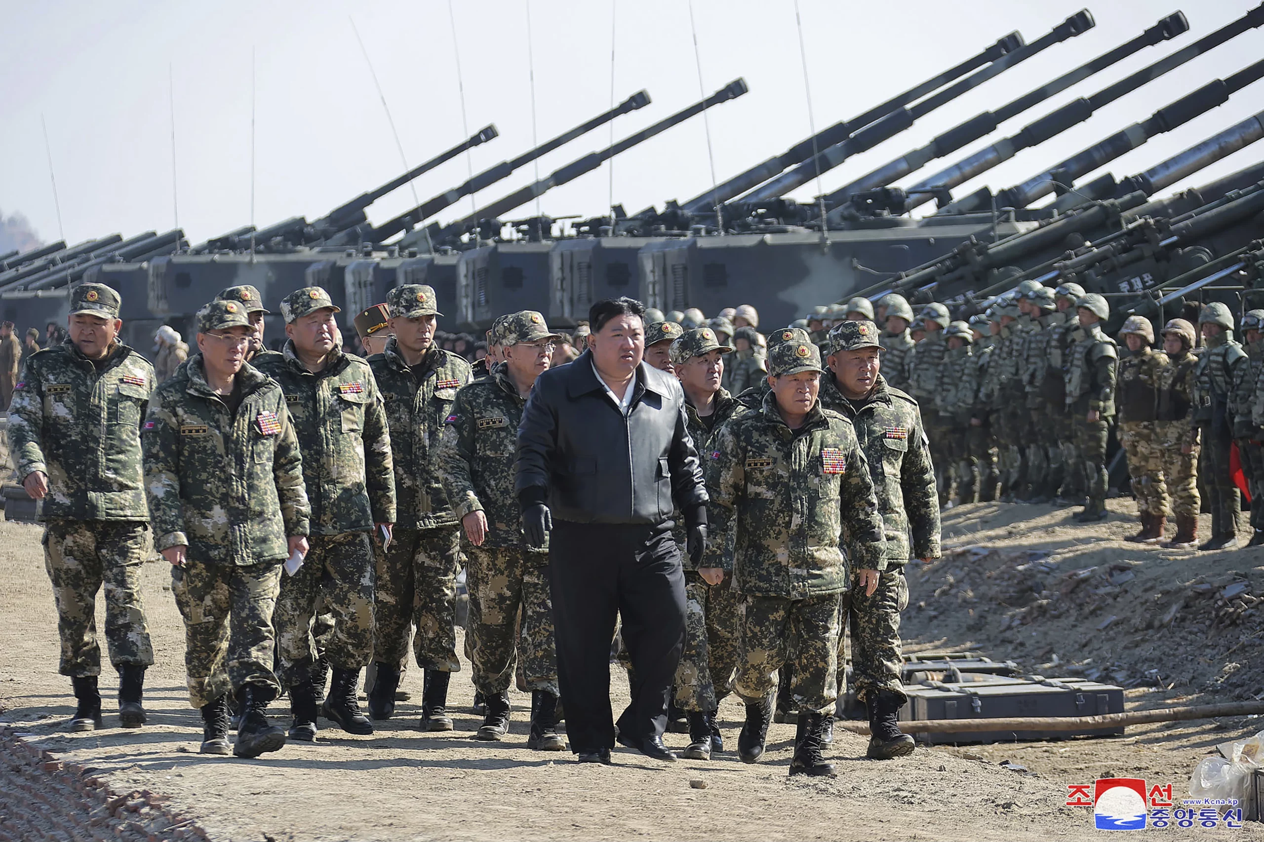 North Korean soldiers in camouflage walking past rows of artillery guns at a military drill