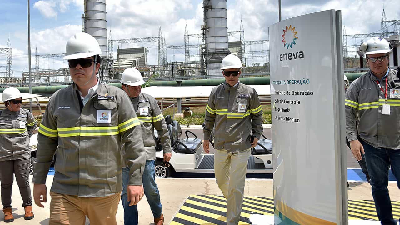 Eneva staff in hard hats walking past a company sign at a thermal power plant in Brazil