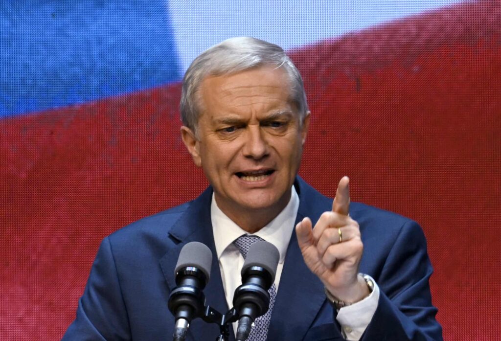 Man speaking at microphones, red and blue background