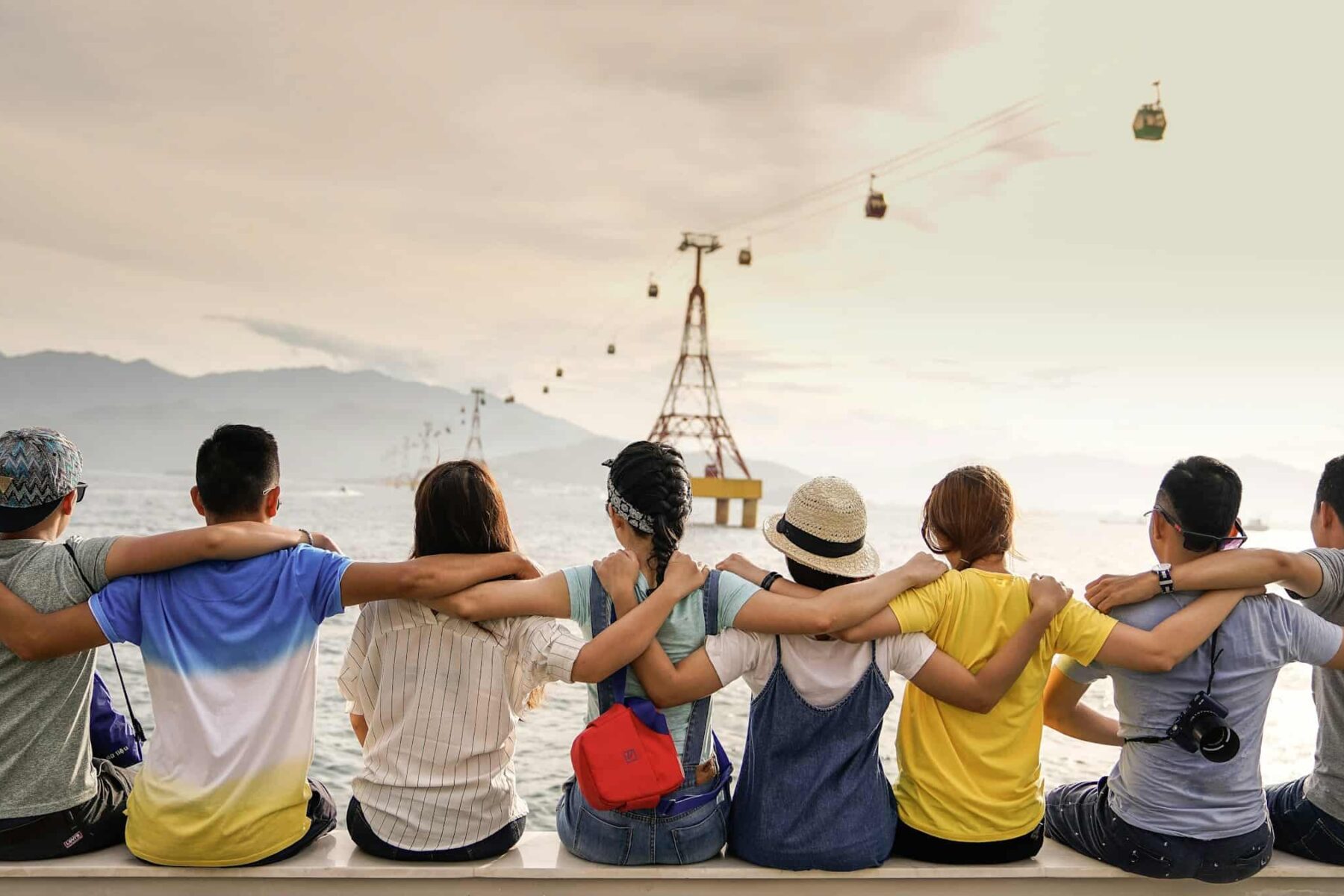 Expat communities in Brazil 2026 — a group of friends sit shoulder-to-shoulder at the waterfront watching a cable-car system reminiscent of Rio de Janeiro