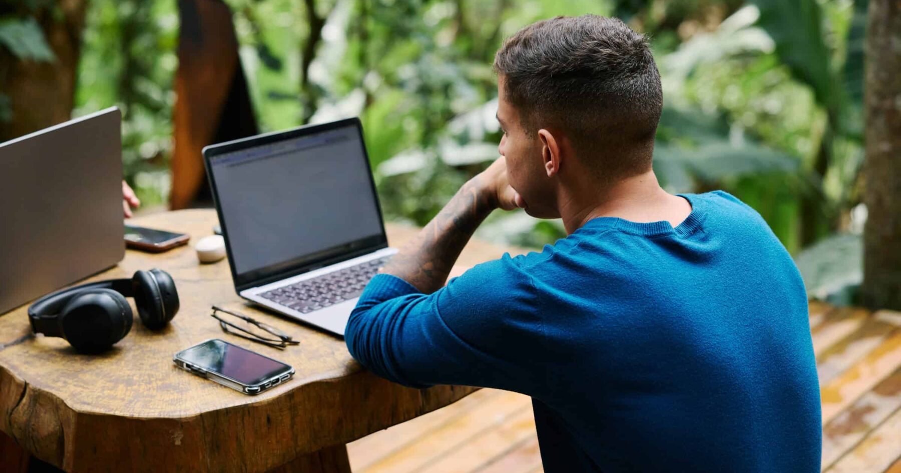 Remote worker at a laptop on a wooden table surrounded by jungle