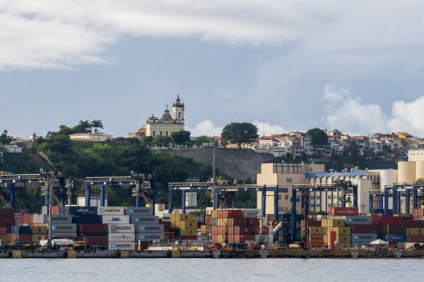 A container ship docked at the port of Santos, Brazil, its cargo silhouetted against the morning sky as global trade disruptions reshape Latin America's economic future.