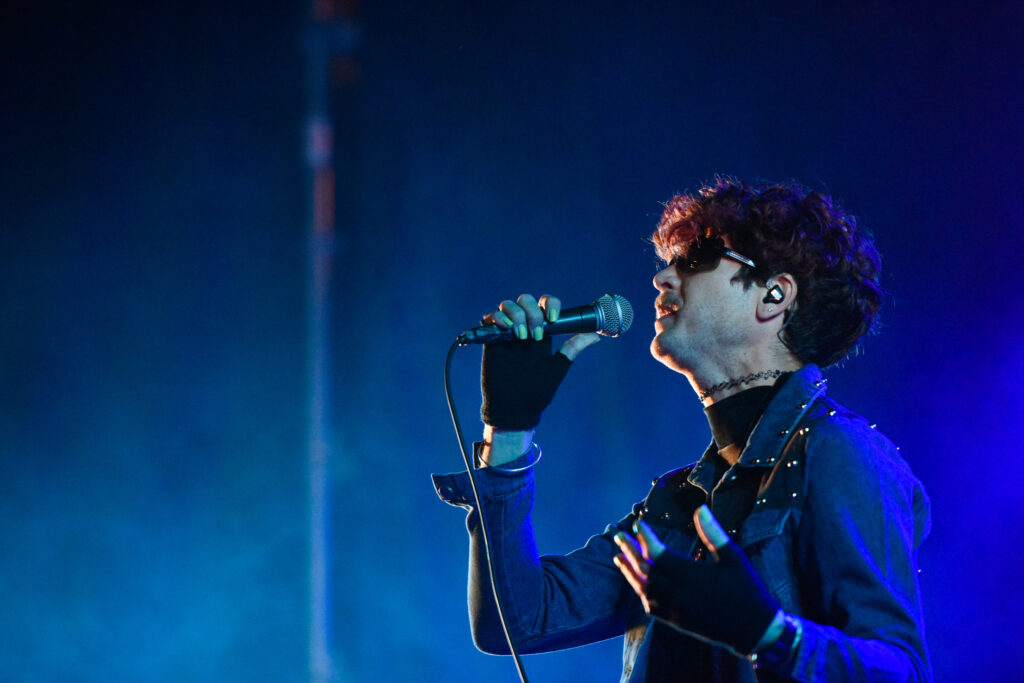 Bandalos Chinos frontman singing into a microphone in blue stage light