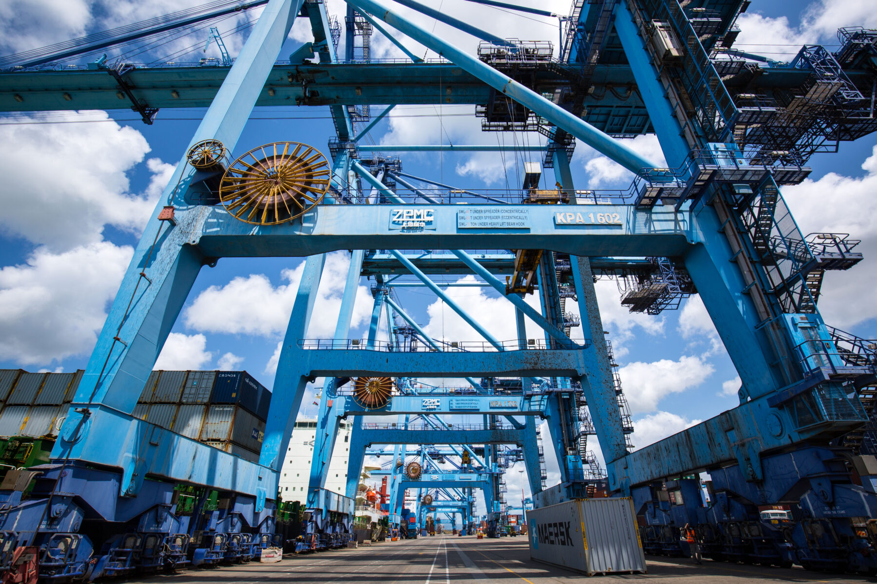 Large blue port cranes and shipping containers under a cloudy sky
