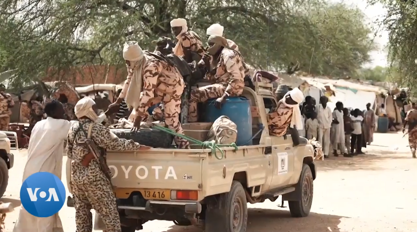 Chadian soldiers in desert camouflage and turbans climb onto a pick-up truck in a dusty town