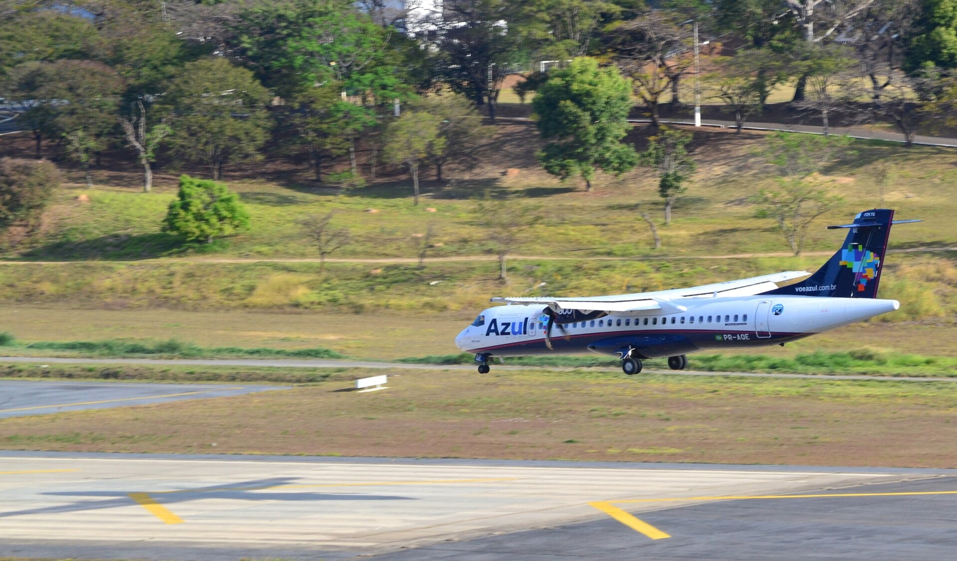 An Azul turboprop aircraft just above a runway, with trees and grass behind it