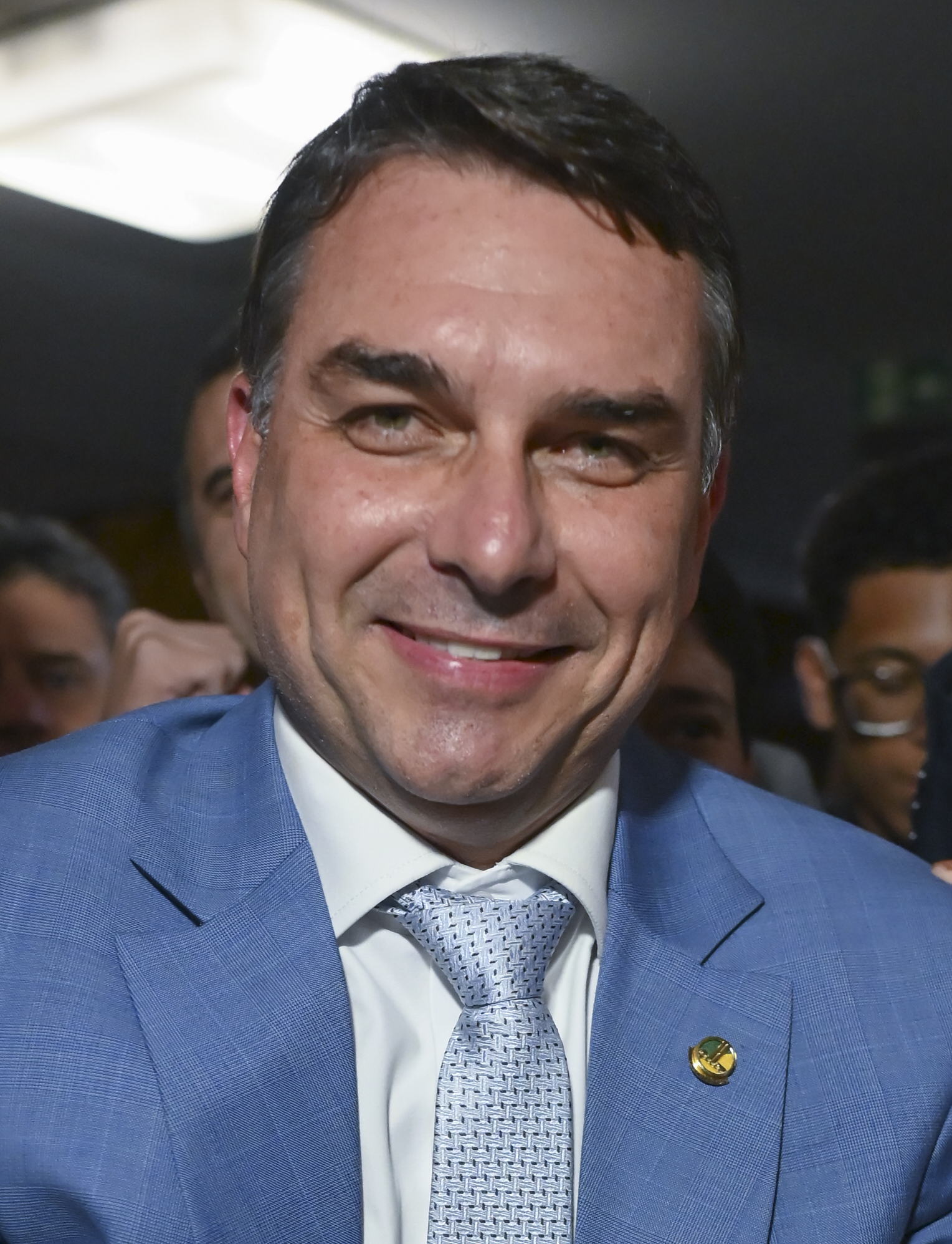 Senator Flávio Bolsonaro smiling in a blue suit at an interview