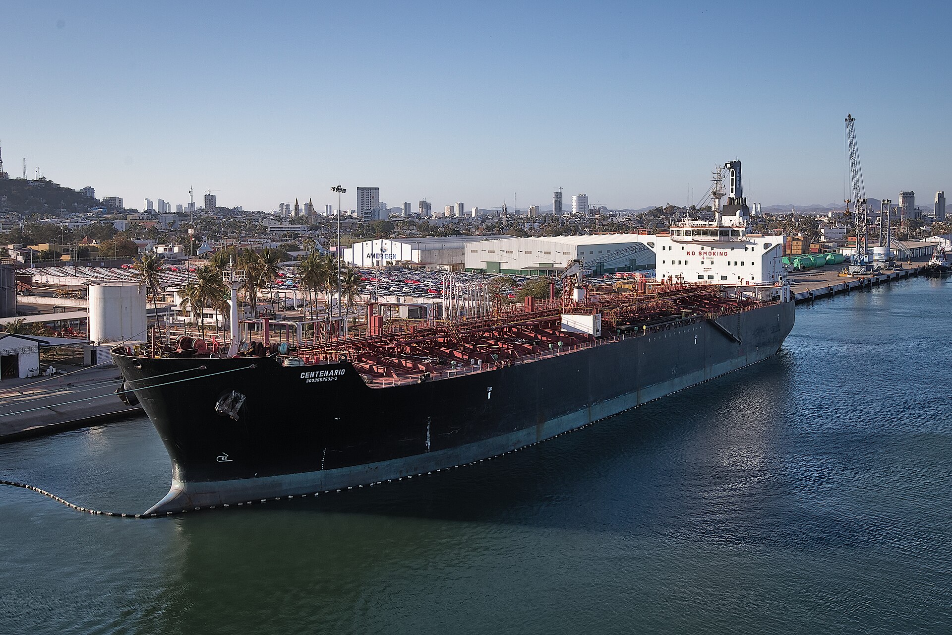 The black-hulled tanker Centenario moored at a port in Mexico with city buildings behind