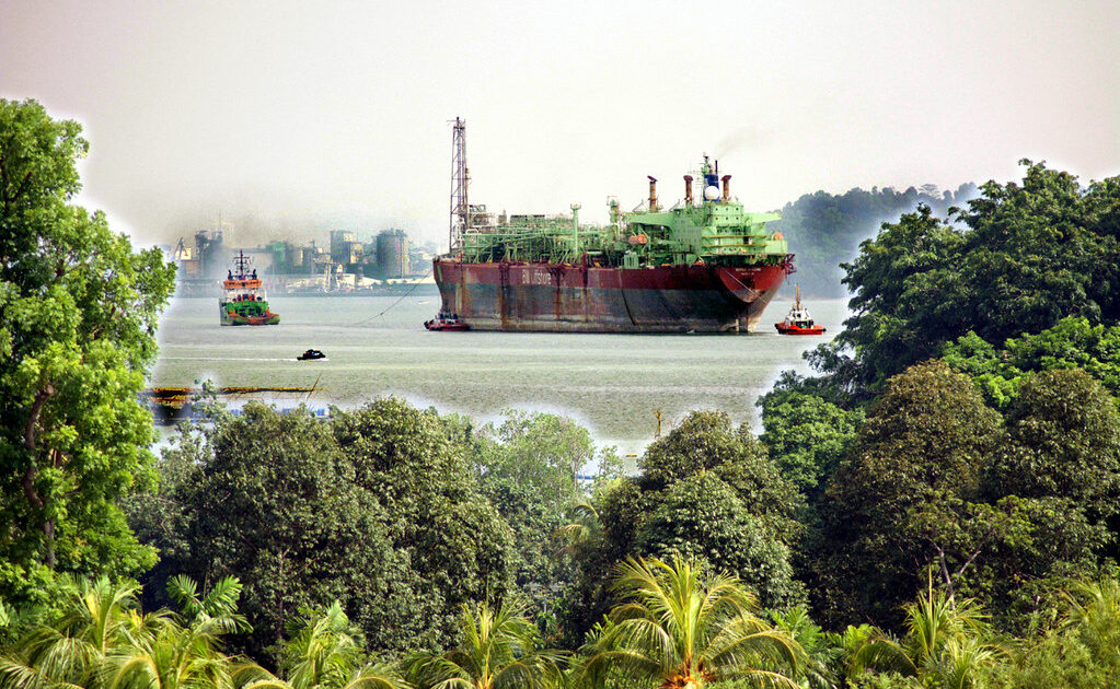 A floating production vessel under tow past a tropical shoreline, illustrating Guyana's fifth offshore project