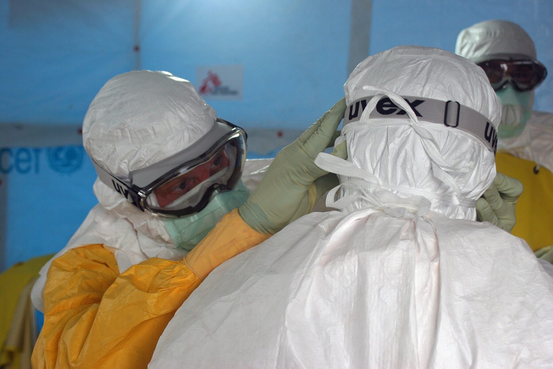 Health workers in white protective suits helping each other adjust goggles at an Ebola treatment tent
