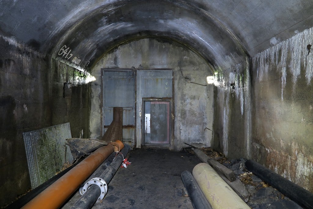 A lit underground tunnel with concrete lining and pipework running along its floor