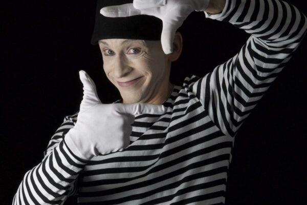 A mime in a striped shirt performs against a black background.