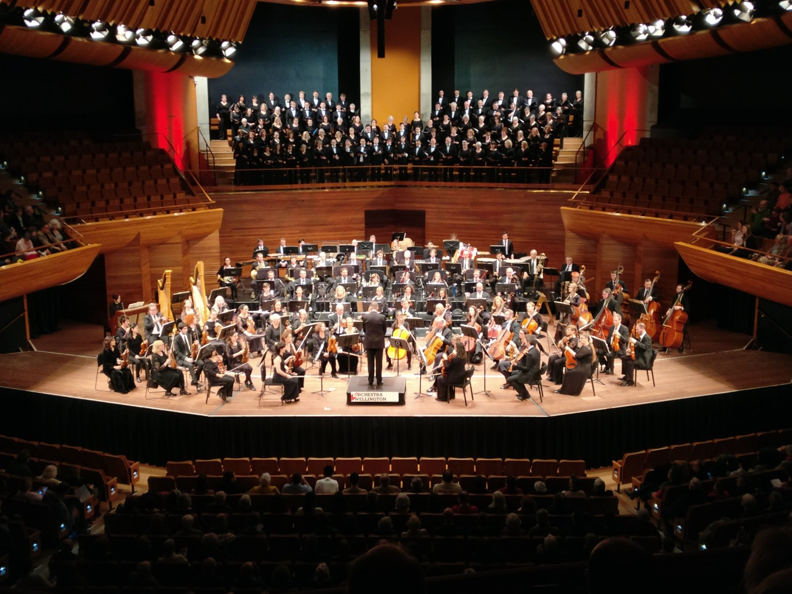 An orchestra and choir perform on a concert stage.