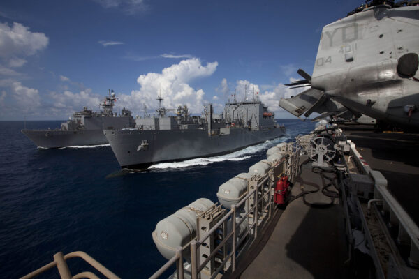 Grey naval vessels under way in formation on open sea under a blue sky