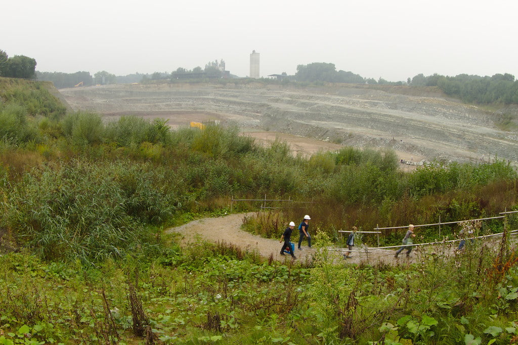 A terraced open-pit quarry with visitors in hard hats walking a path along its rim