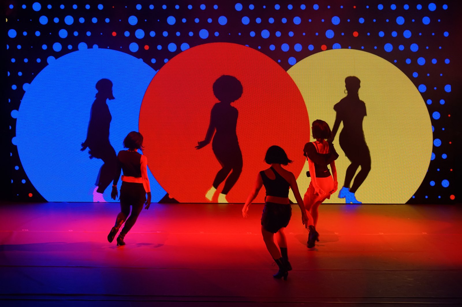 Performers on a brightly lit contemporary stage.