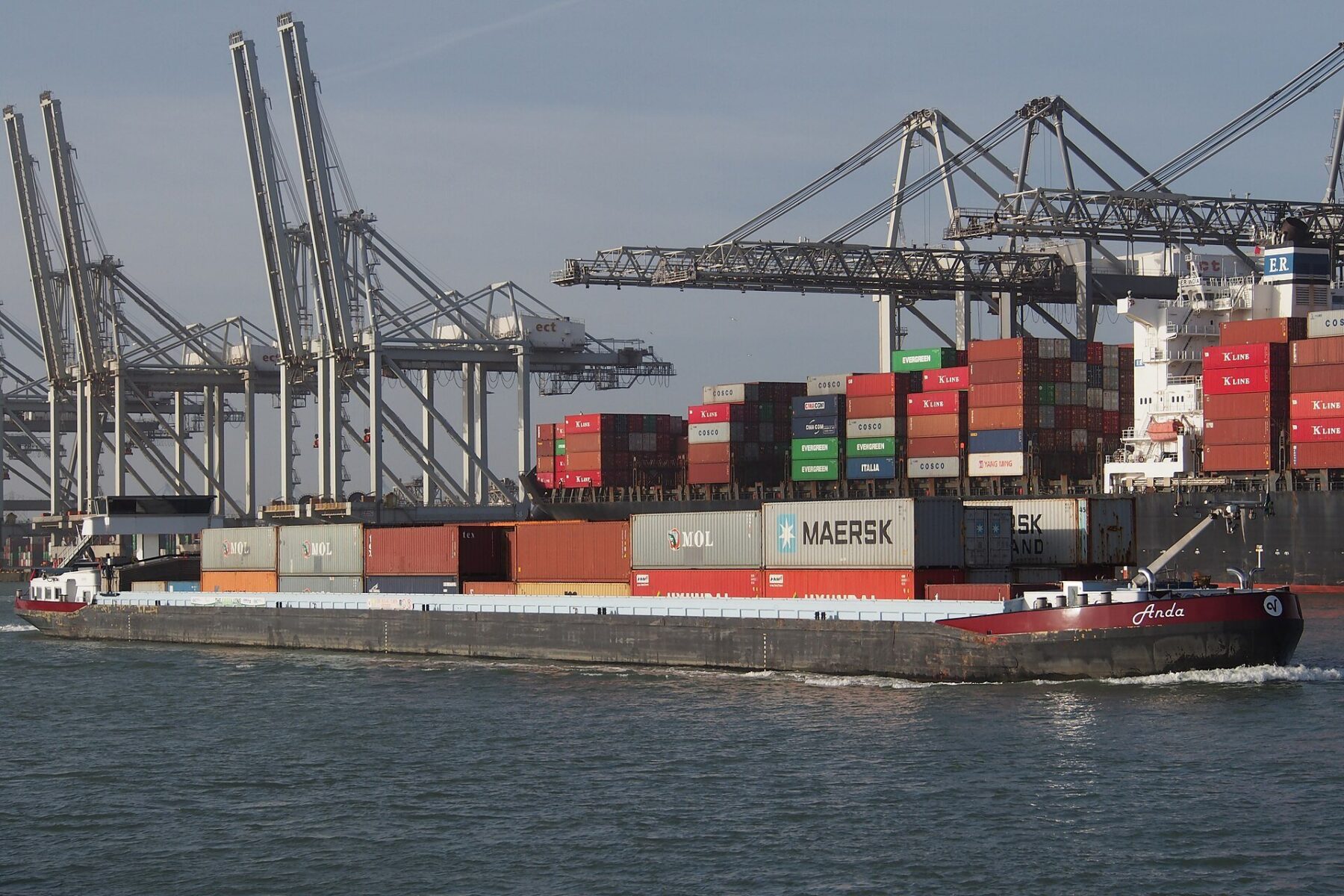 A container ship and barge at a busy port, illustrating the transshipment of goods that the US says is used to dodge tariffs.