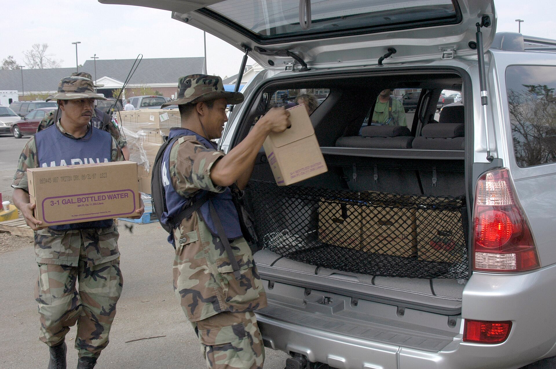 Two Mexican Navy sailors carrying boxes of bottled water to a vehicle