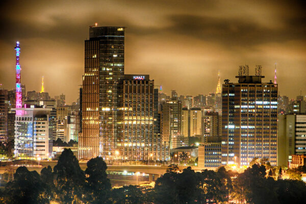 The São Paulo skyline lit up after dark, towers and avenues seen across the treeline