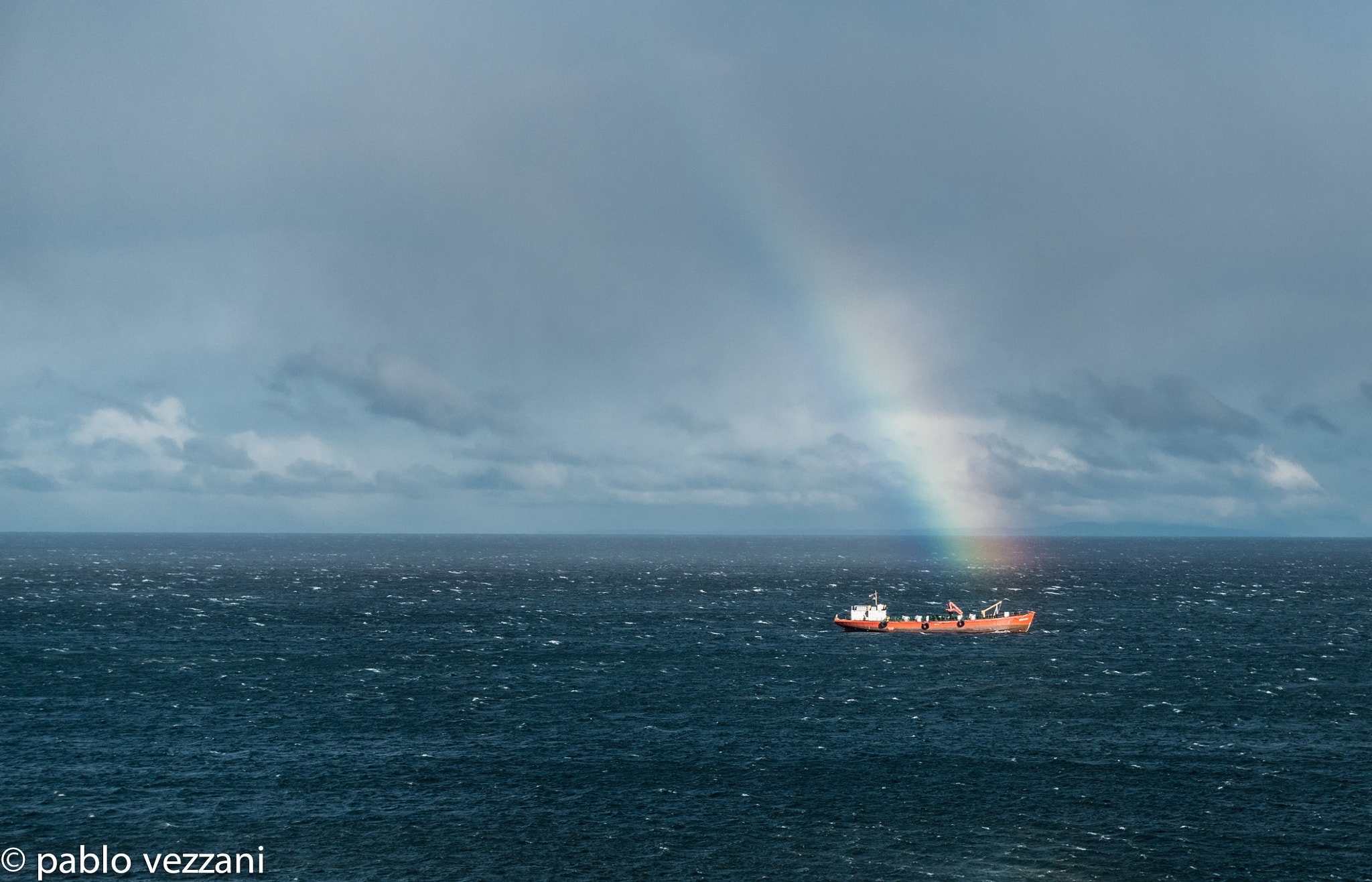 A vessel crosses the Strait of Magellan under a rainbow