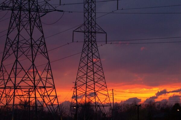 Two high-voltage transmission pylons silhouetted against an orange sunset sky