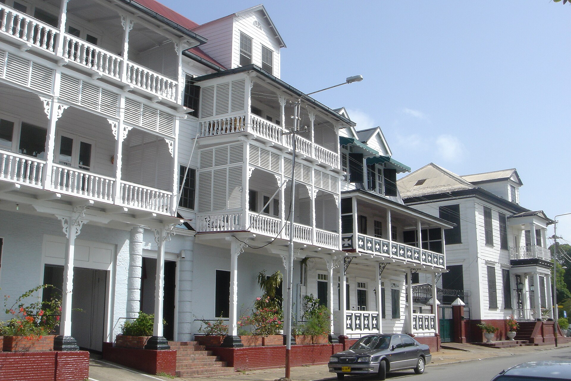 A row of white painted wooden colonial buildings with shuttered balconies along a street in the historic inner city of Paramaribo