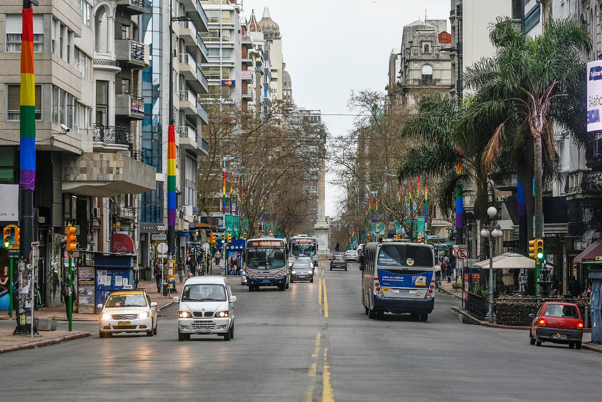 Traffic and buses on Avenida 18 de Julio in central Montevideo, lined with apartment buildings and palm trees